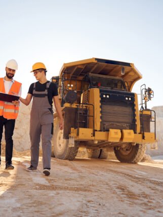 Standing near haul truck and talking about document. Two men in uniform are working together in the quarry.